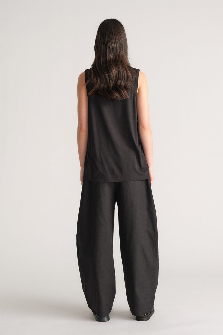 Woman wearing a relaxed black sleeveless tank paired with wide-leg black pants, standing against a neutral backdrop