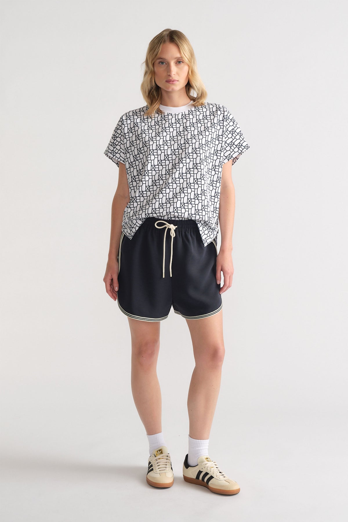 Woman wearing a relaxed black and white monogram tee paired with black drawstring shorts and retro sneakers for casual style.