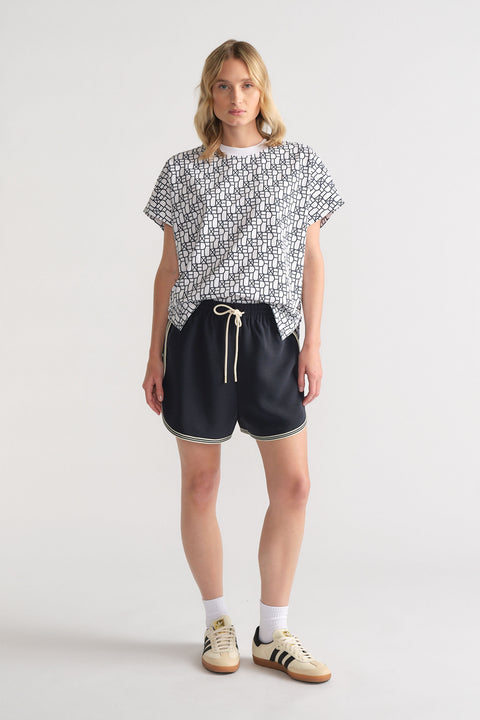 Woman wearing a relaxed black and white monogram tee paired with black drawstring shorts and retro sneakers for casual style.