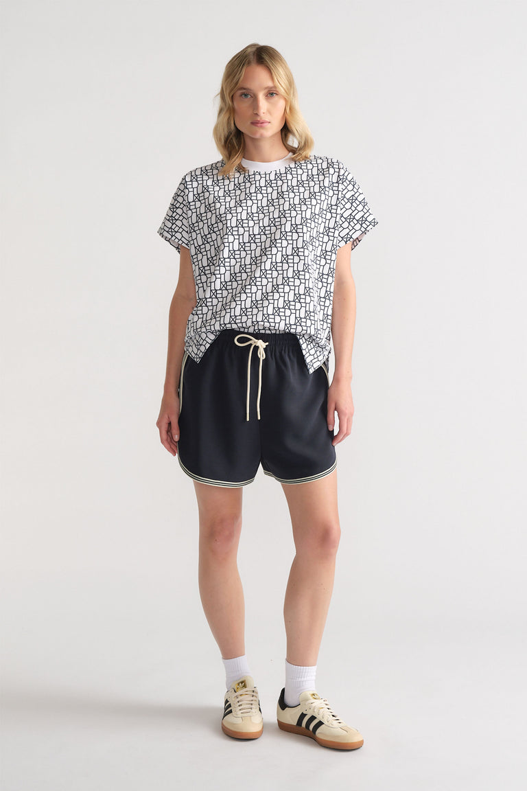 Woman wearing a relaxed black and white monogram tee paired with black drawstring shorts and retro sneakers for casual style.