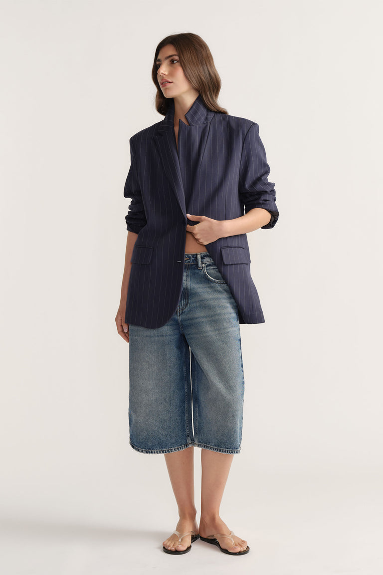 Woman wearing D-Luxe Denim Long Line Short in mid-blue denim styled with a navy pinstripe blazer by Decjuba Australian brand
