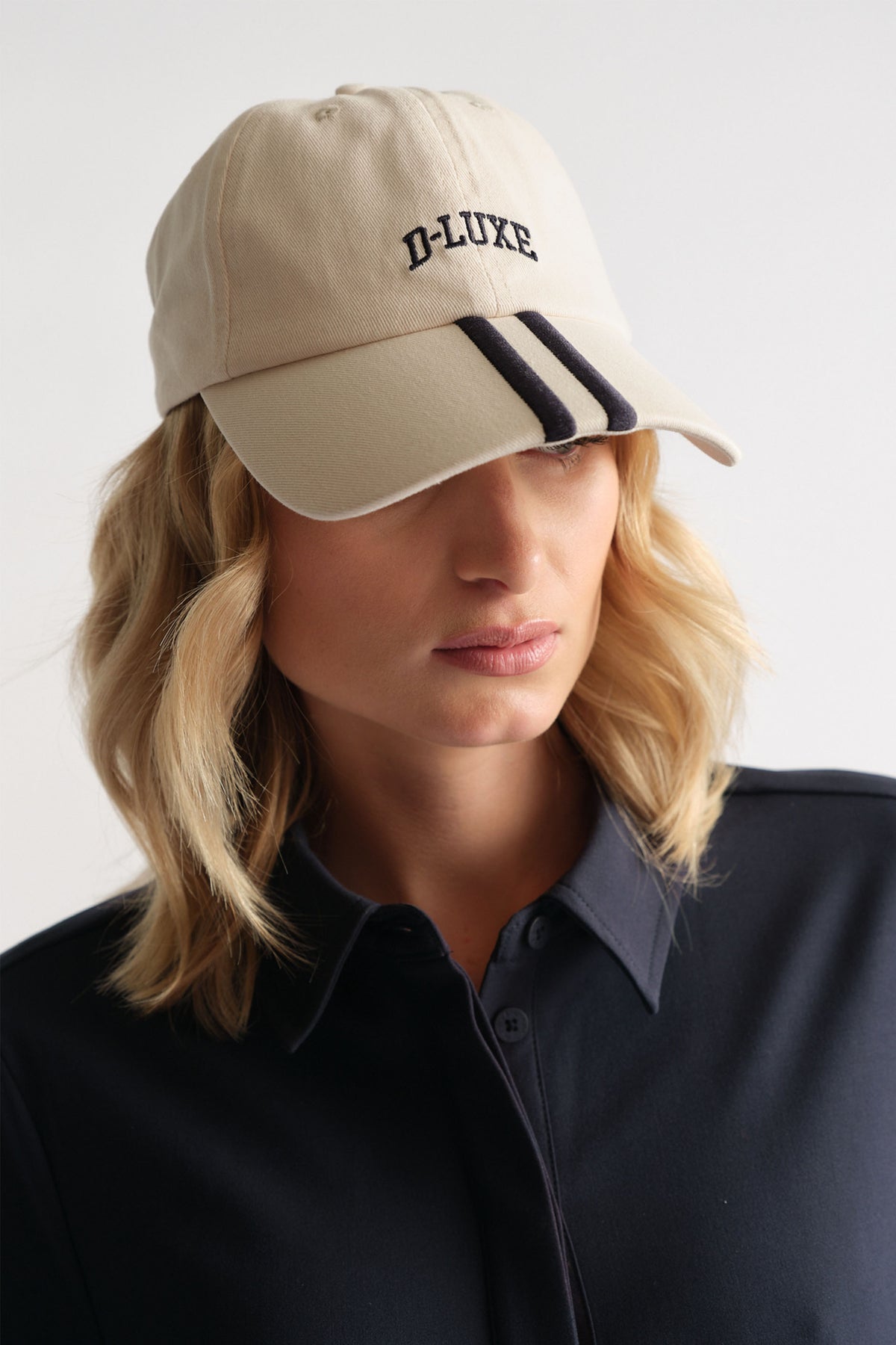 Woman wearing a beige cap with black stripes and embroidery paired with a navy collared top for a casual look