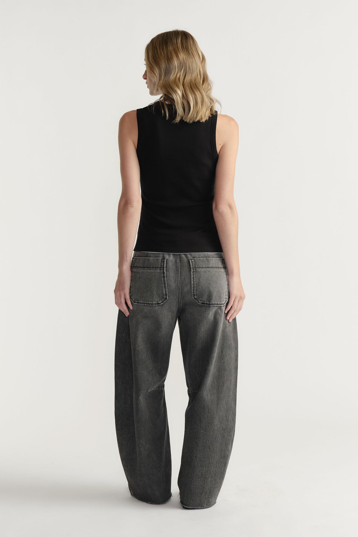 Woman seen from behind wearing a fitted black ribbed tank top paired with relaxed wide-leg dark grey jeans