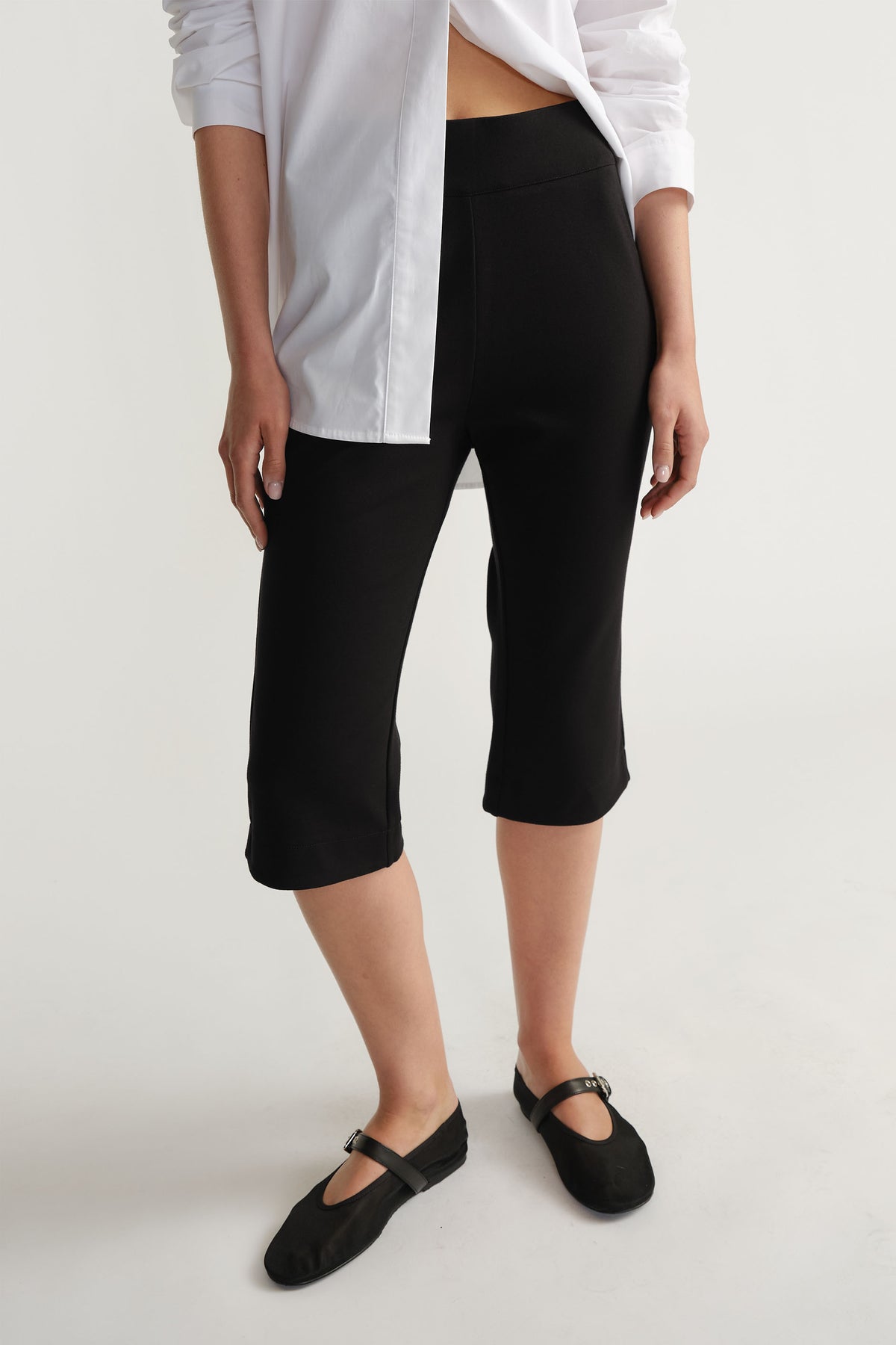 Woman wearing fitted black capri pants paired with a crisp white shirt and simple black flats for a chic look