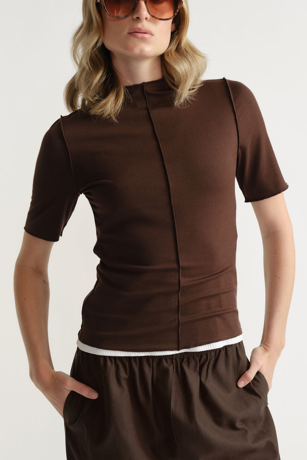 Portrait of model wearing fitted brown D-Luxe Short Sleeve Top with mock neck and centre front seam, gallery position 2