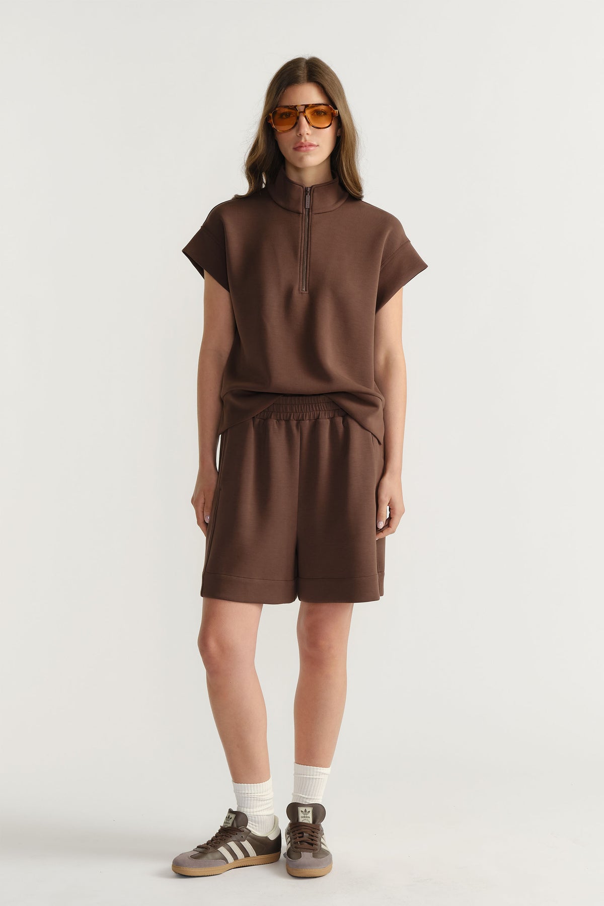 Woman wearing a relaxed brown half-zip neoprene top with matching shorts, paired with white socks and sneakers