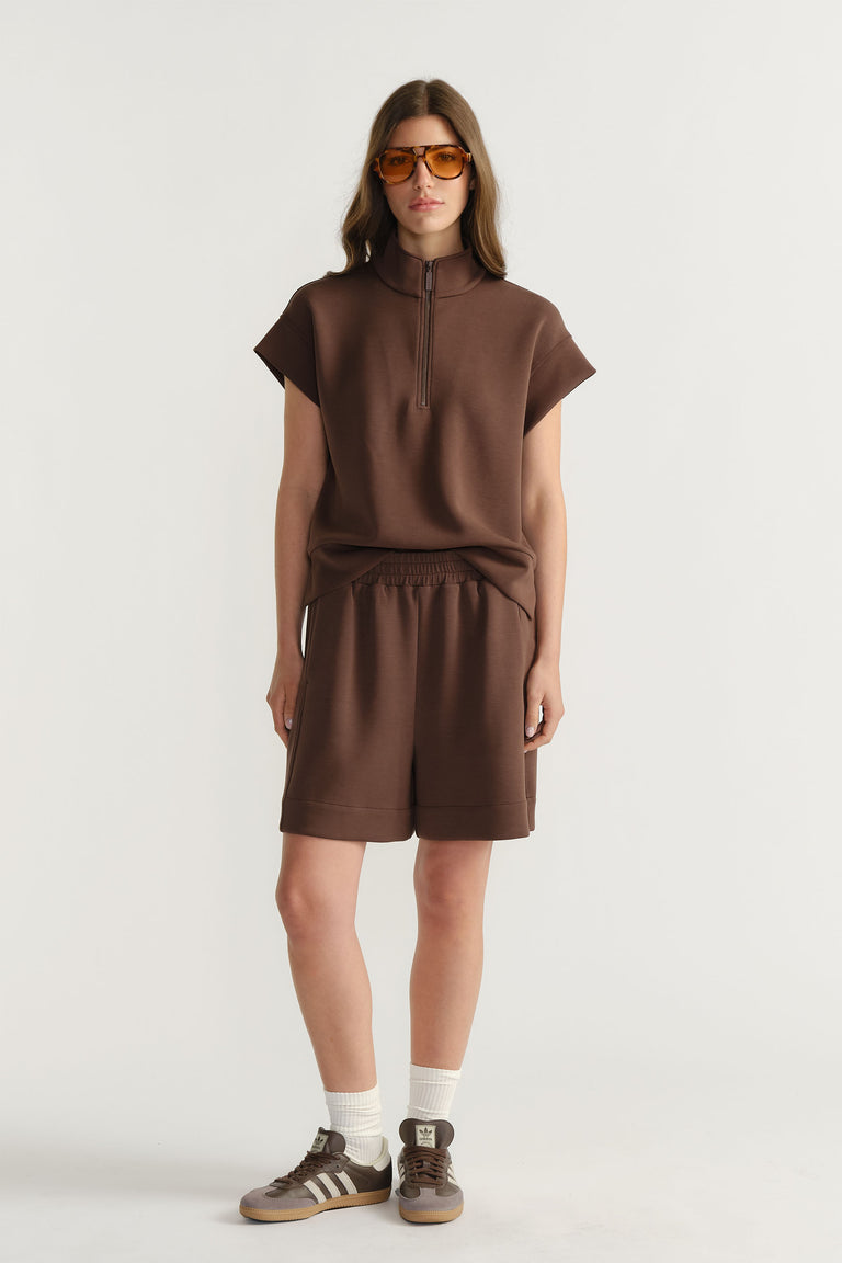 Woman wearing a relaxed brown half-zip neoprene top with matching shorts, paired with white socks and sneakers
