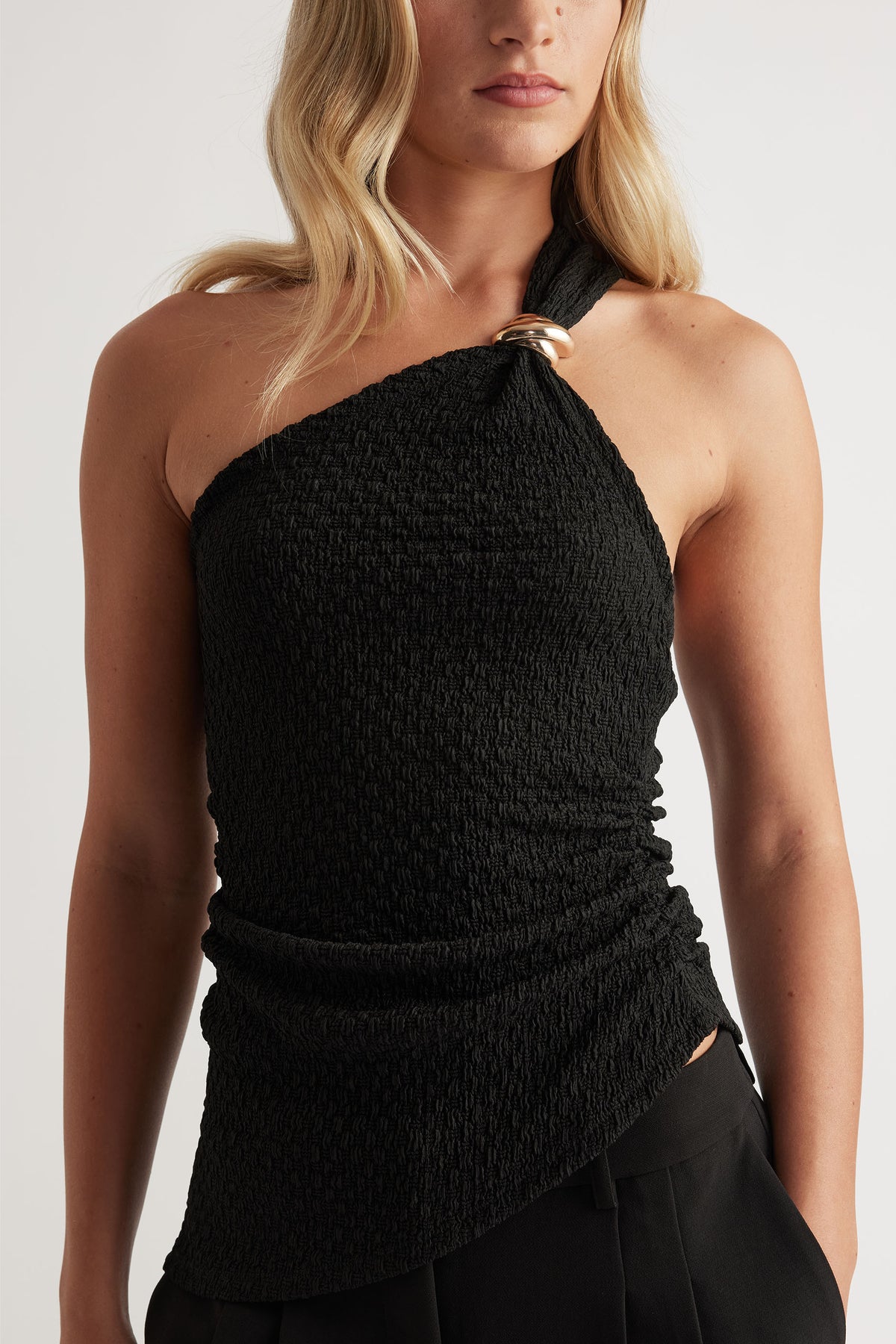 Textured black one-shoulder tank with gold ring detail and an asymmetrical hem for a modern, chic silhouette.