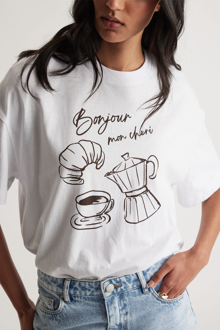 Woman wearing a white tee with French café-inspired print paired with light blue denim jeans for a casual look