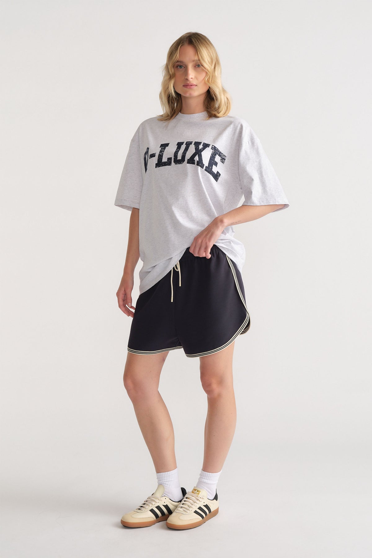 Woman wearing an oversized grey tee with bold lettering paired with relaxed black shorts and casual sneakers