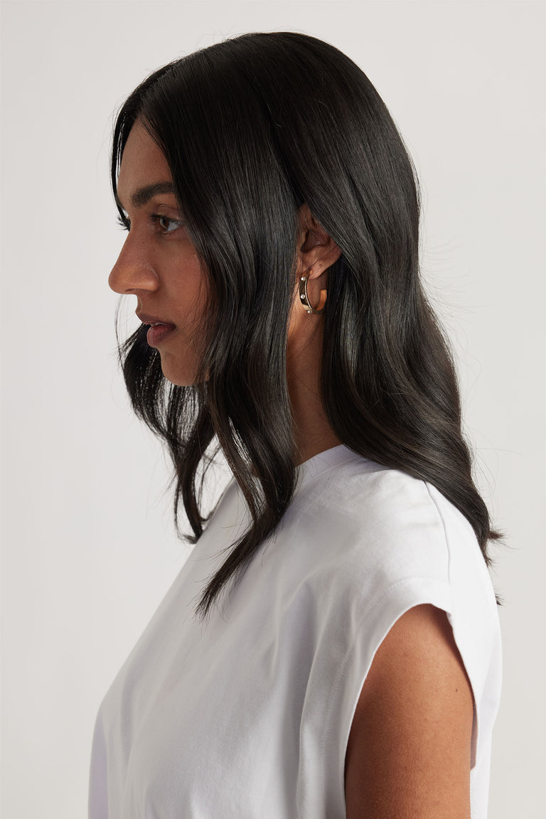 Profile of woman with long dark hair wearing a white sleeveless top and gold hoop earrings with delicate diamanté accents.