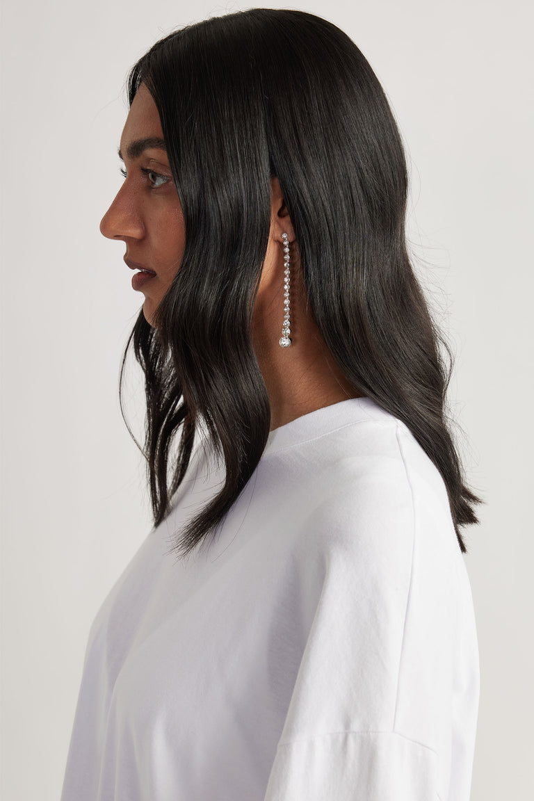 Profile of woman with long dark hair wearing a dangling silver earring with sparkling stones and a white top