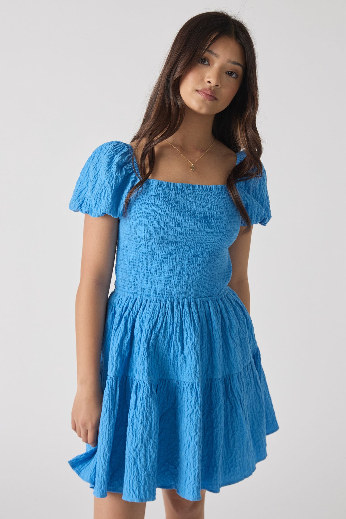 Girl wearing a bright blue textured mini dress with puff sleeves and a tiered skirt, styled for casual elegance.