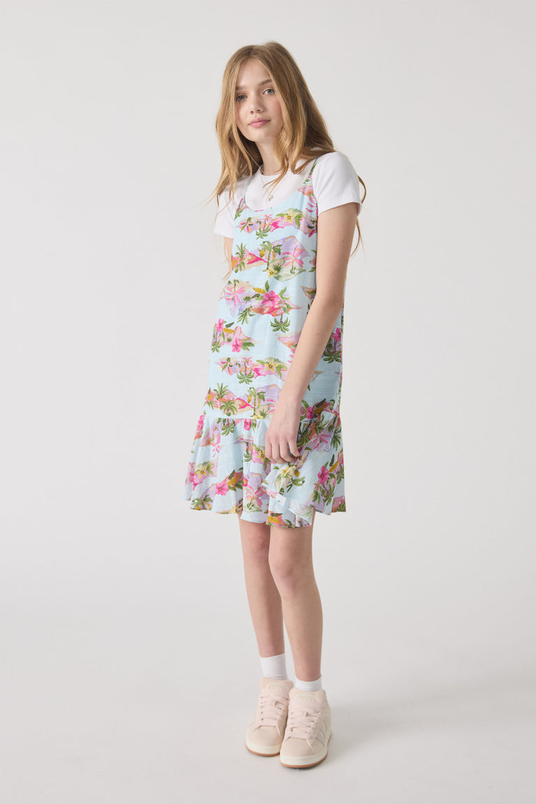 Teen girl wearing a pastel floral strappy dress layered over a white tee, paired with light sneakers and socks
