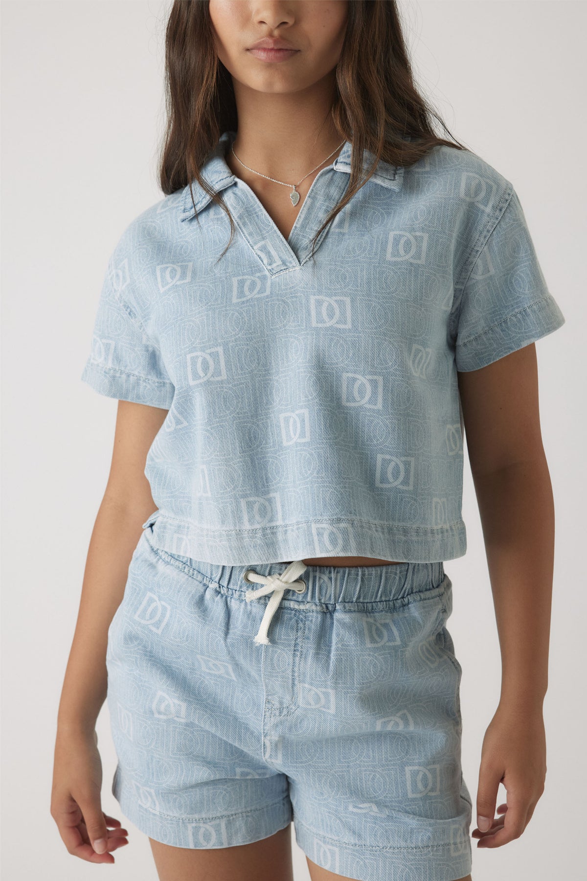 Girl wearing a light blue denim shirt with subtle monogram print paired with matching drawstring shorts for a casual look