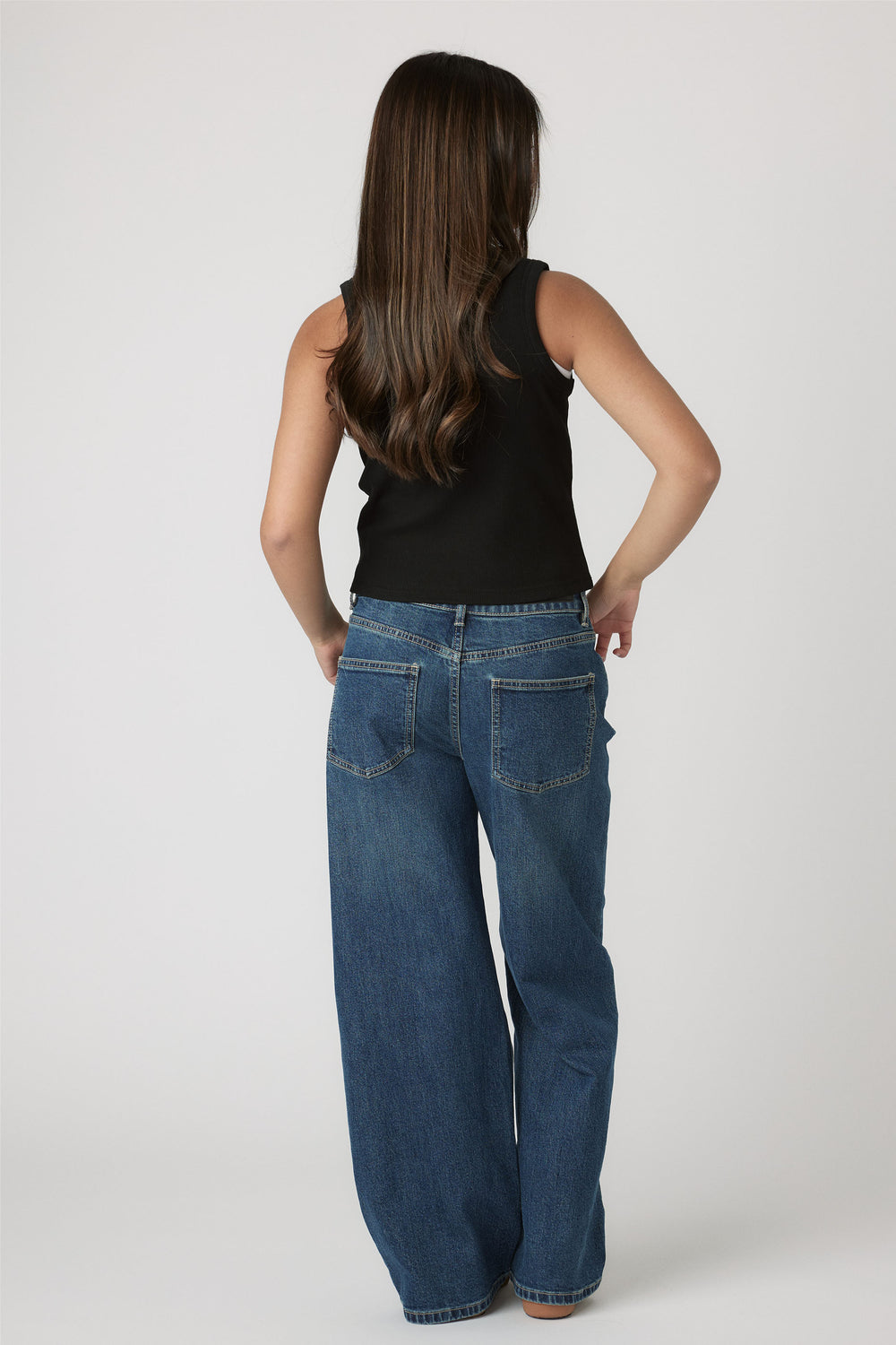 Girl seen from behind wearing a black Girls Harper Logo Tank paired with relaxed blue denim jeans by Decjuba Australian brand