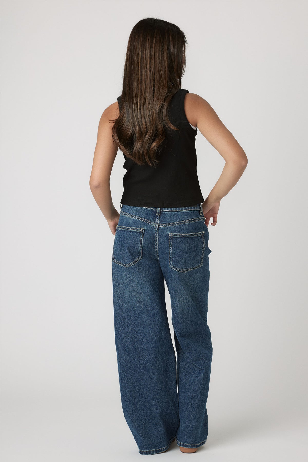 Girl seen from behind wearing a black Girls Harper Logo Tank paired with relaxed blue denim jeans by Decjuba Australian brand