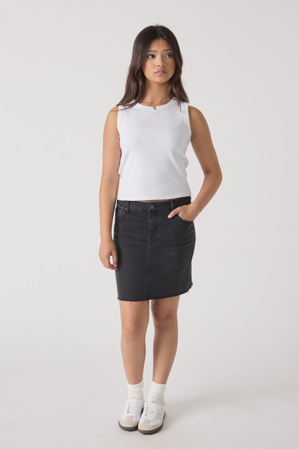 Teen girl wearing white Girls Harper Logo Tank styled with black denim skirt and sneakers by Decjuba Australian fashion brand