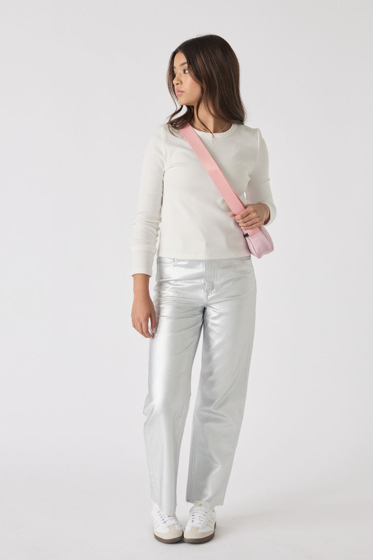 Teen girl wearing a white long-sleeve top with silver straight-leg jeans and white sneakers, carrying a pink crossbody bag