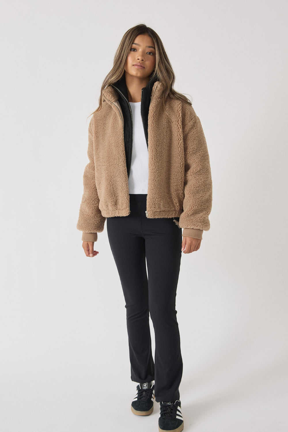 Teen girl wearing slim-fit black yoga pants paired with a white top and a cozy camel fleece jacket for casual comfort.