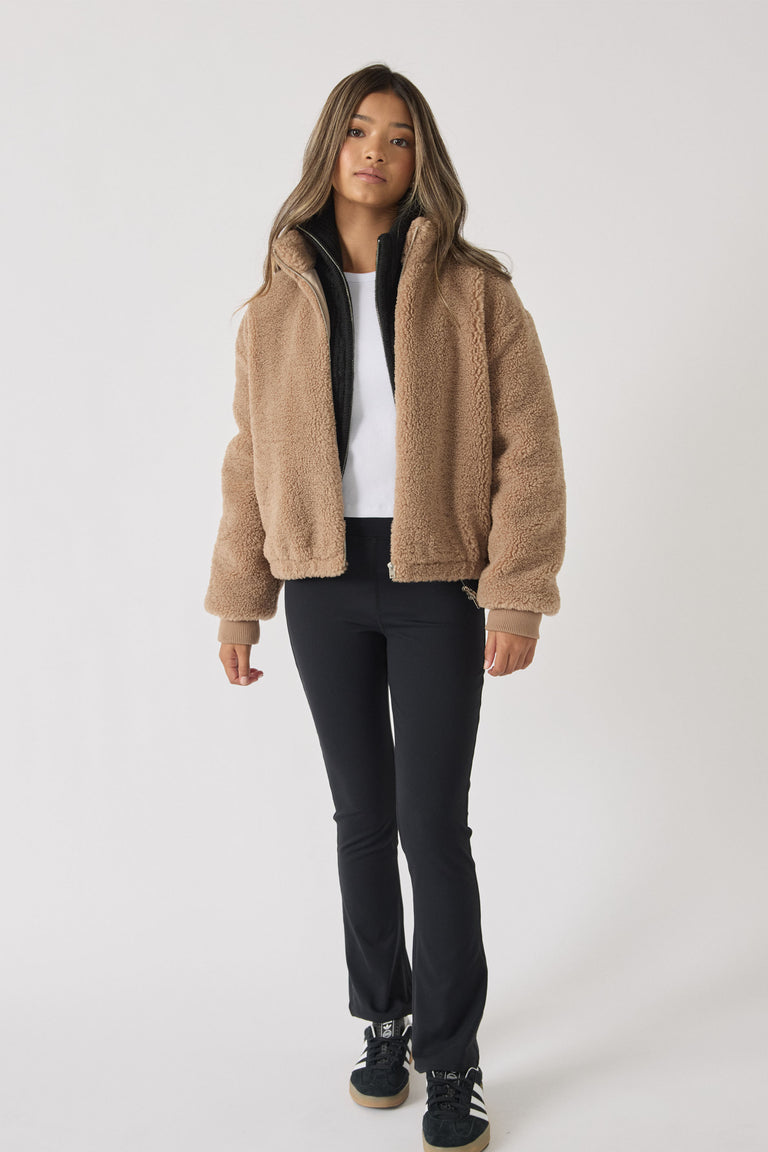 Teen girl wearing slim-fit black yoga pants paired with a white top and a cozy camel fleece jacket for casual comfort.
