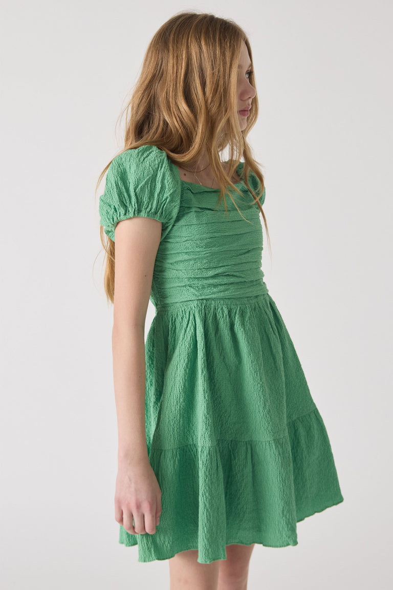Girl wearing a textured spring green mini dress with puff sleeves and a gathered bodice for a playful look