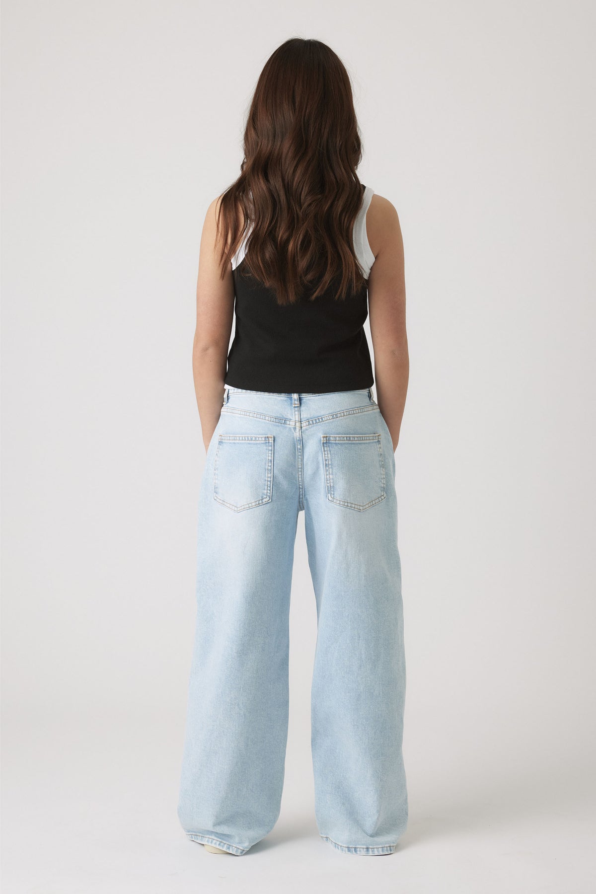 Back view of girl wearing light wash wide-leg jeans paired with a black and white layered tank top