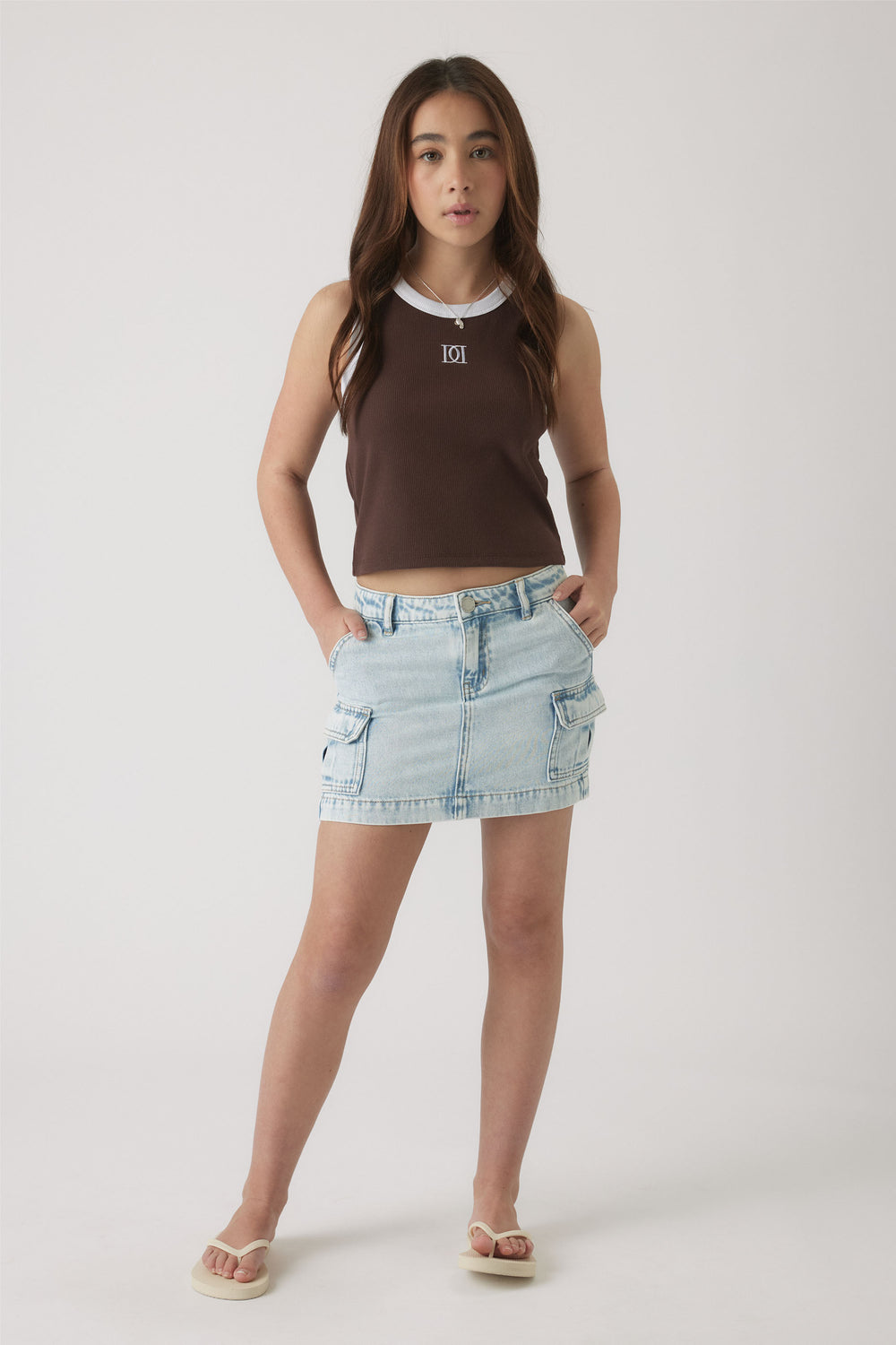 Teen girl wearing a sleeveless brown tank with white trim, paired with a light wash denim skirt with cargo pockets.