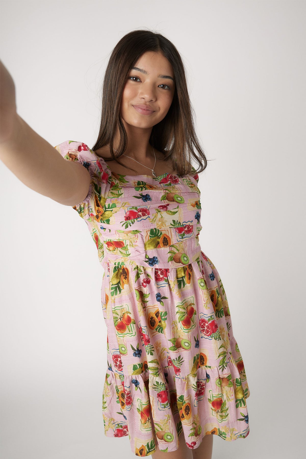 Girl wearing a pink mini dress with colorful fruit prints, puff sleeves, and a gathered waist for a playful look