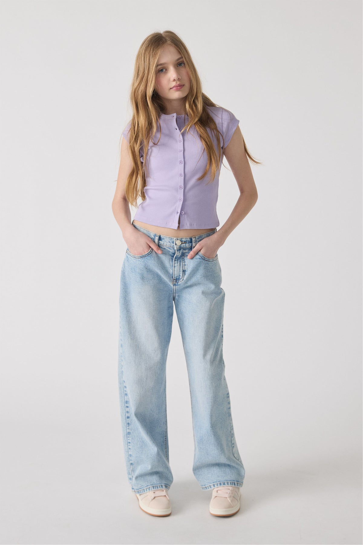 Teen girl wearing a lilac ribbed button-up top paired with relaxed light wash denim jeans and cream sneakers.