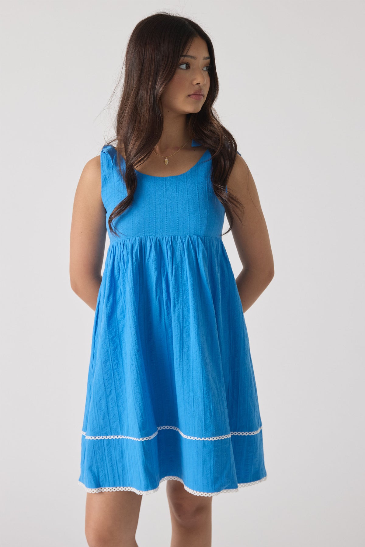 Girl wearing a vibrant blue mini dress with subtle textured pattern and delicate lace trim details at the hem.