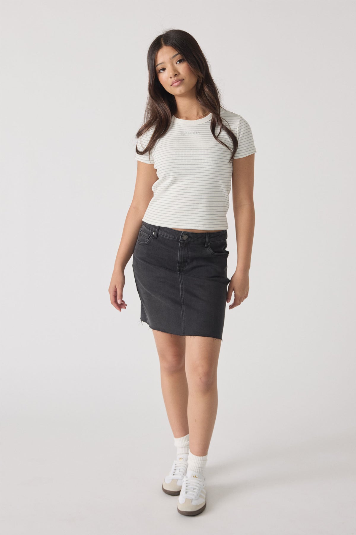 Young woman wearing a fitted striped crop tee paired with a black denim skirt and white sneakers in a casual look.