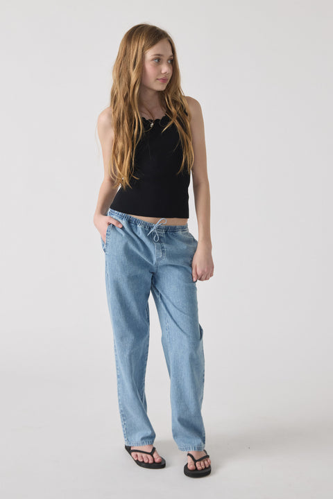 Girl wearing relaxed light blue denim pants with a drawstring waist, paired with a black sleeveless top and sandals.