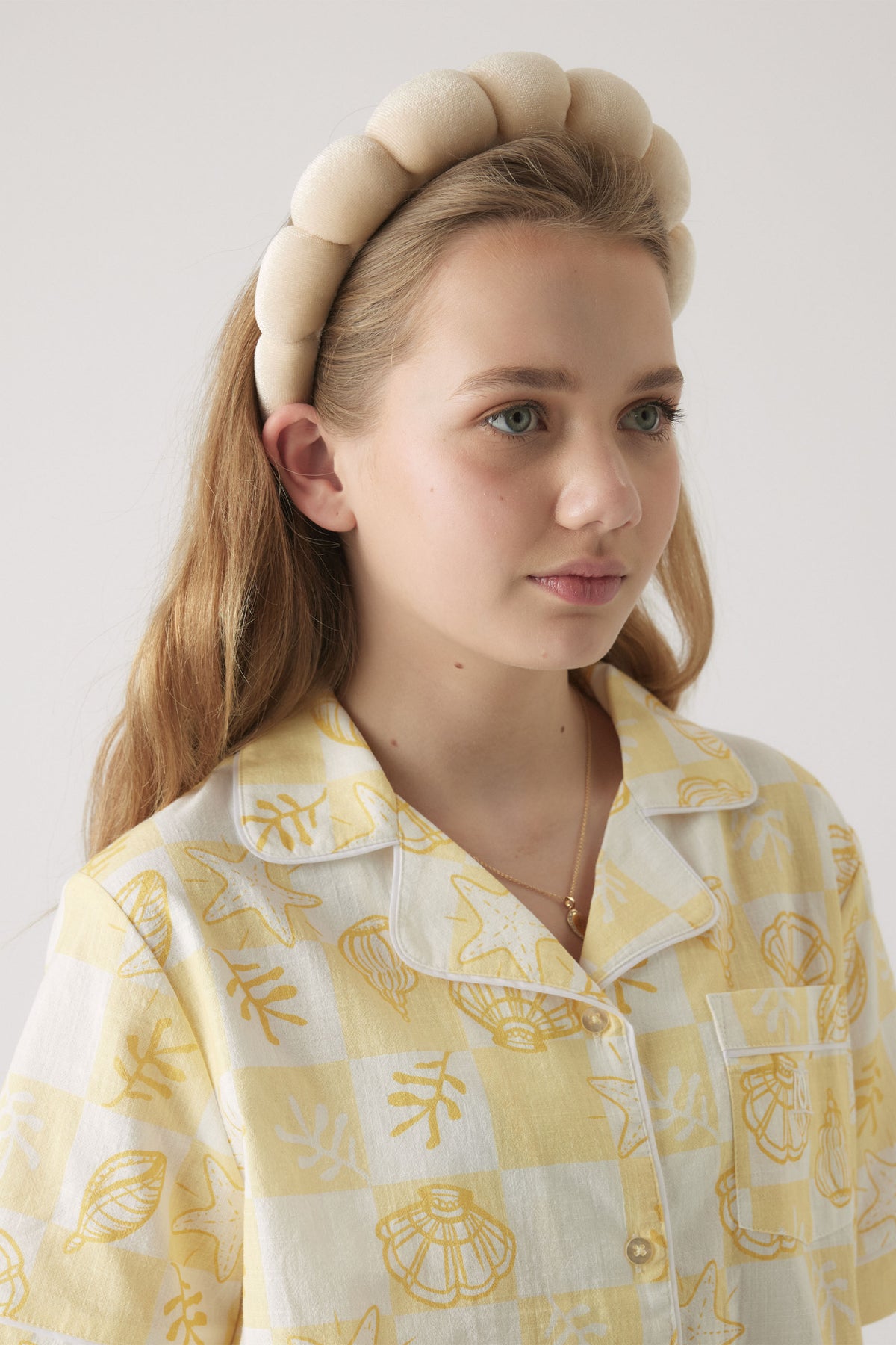 Young girl wearing a soft beige padded headband paired with a yellow and white patterned button-up shirt.