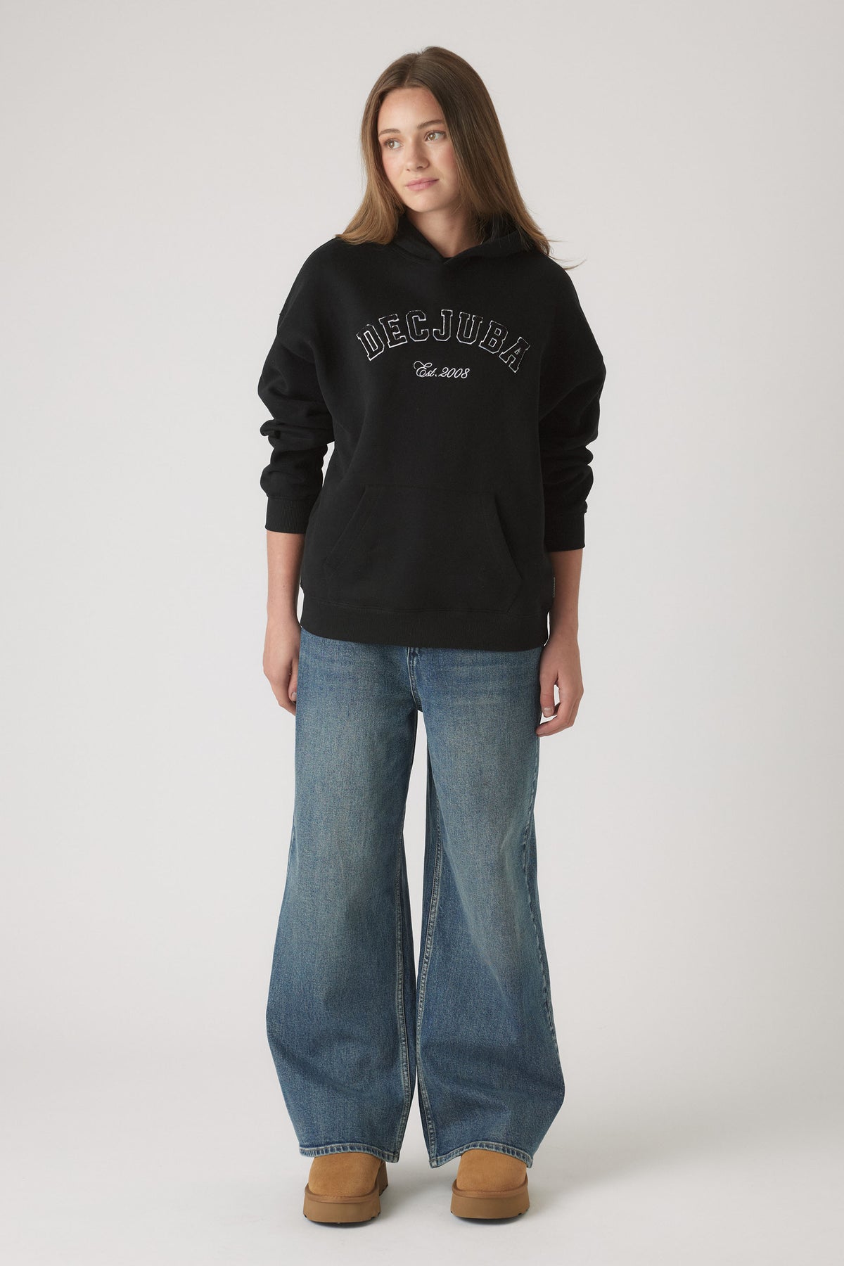 Young woman wearing a relaxed black hoodie with front logo paired with wide-leg medium wash denim jeans and tan boots