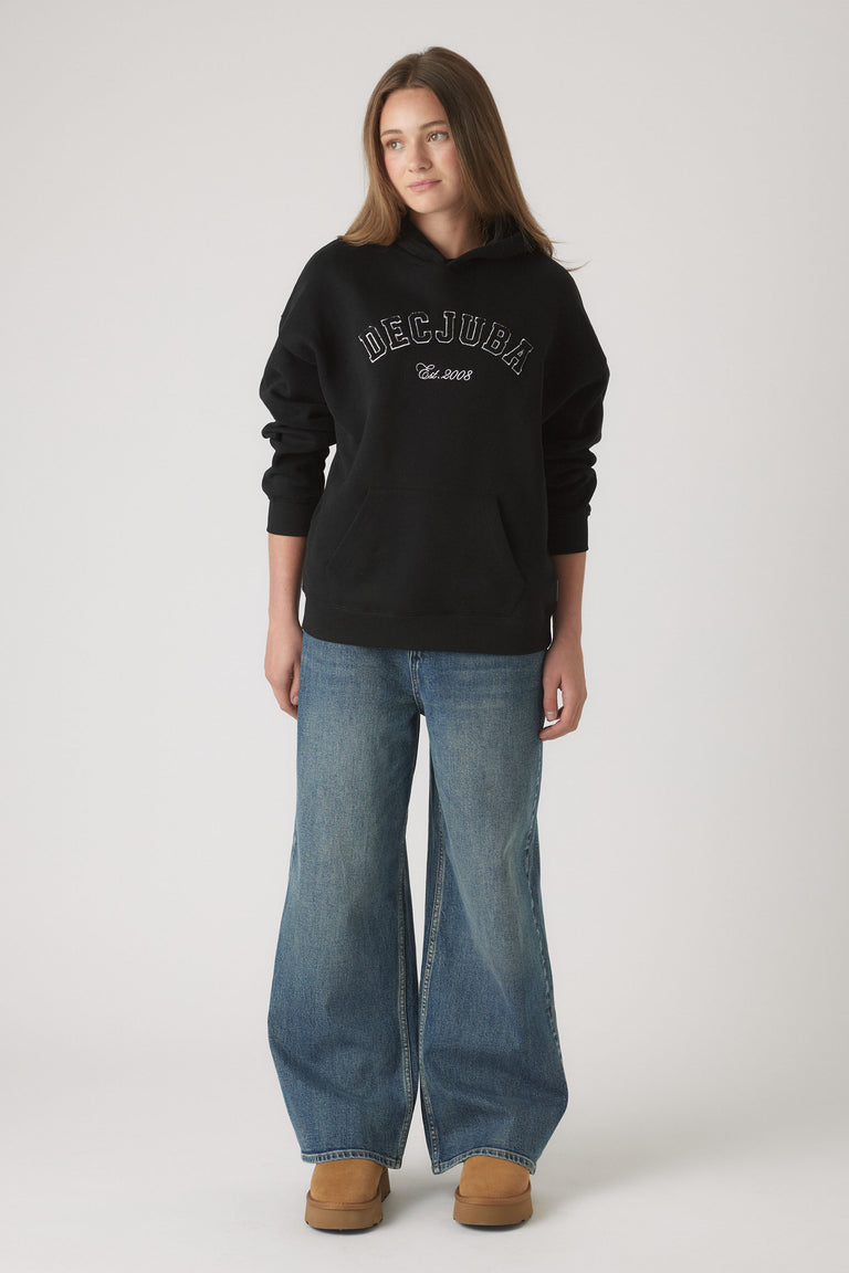 Young woman wearing a relaxed black hoodie with front logo paired with wide-leg medium wash denim jeans and tan boots