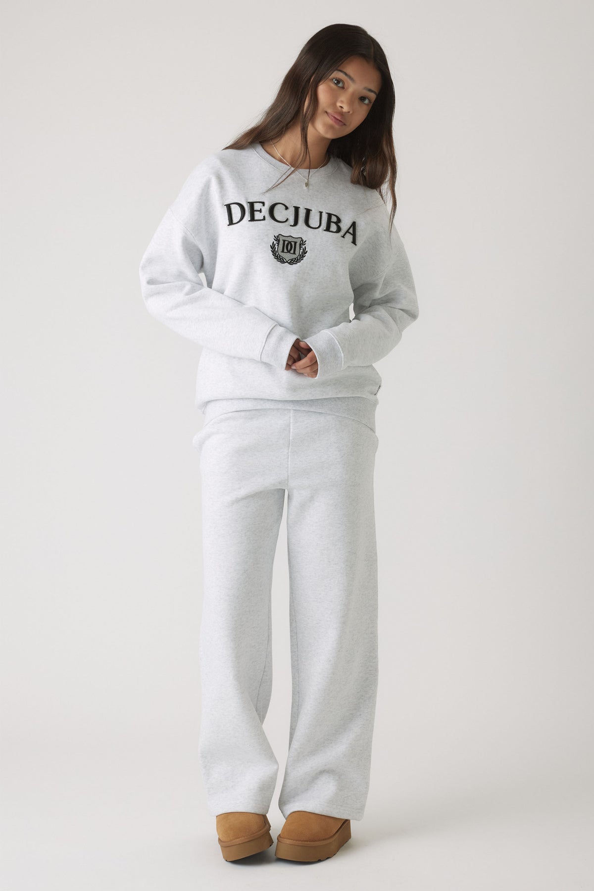Young woman wearing light grey rolled waist track pants paired with a matching sweatshirt and tan slip-on shoes