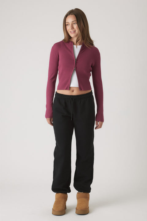 Girl wearing relaxed black track pants with elastic cuffs paired with a fitted berry zip-up cardigan and tan boots
