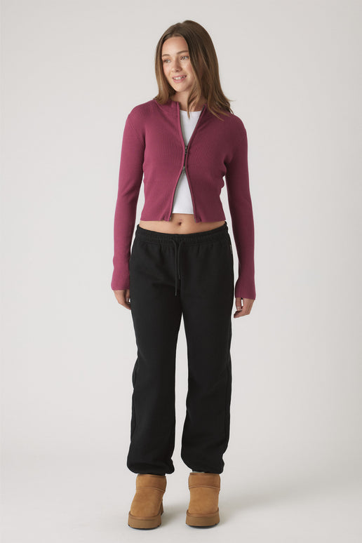 Girl wearing relaxed black track pants with elastic cuffs paired with a fitted berry zip-up cardigan and tan boots