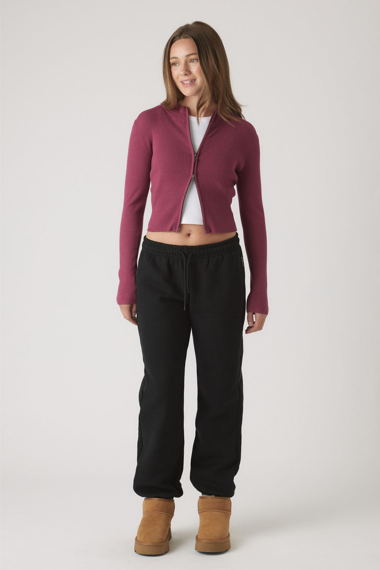 Girl wearing relaxed black track pants with elastic cuffs paired with a fitted berry zip-up cardigan and tan boots