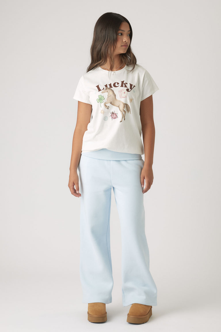 Girl wearing a white embellished tee with lucky charms paired with relaxed light blue wide-leg pants and brown boots
