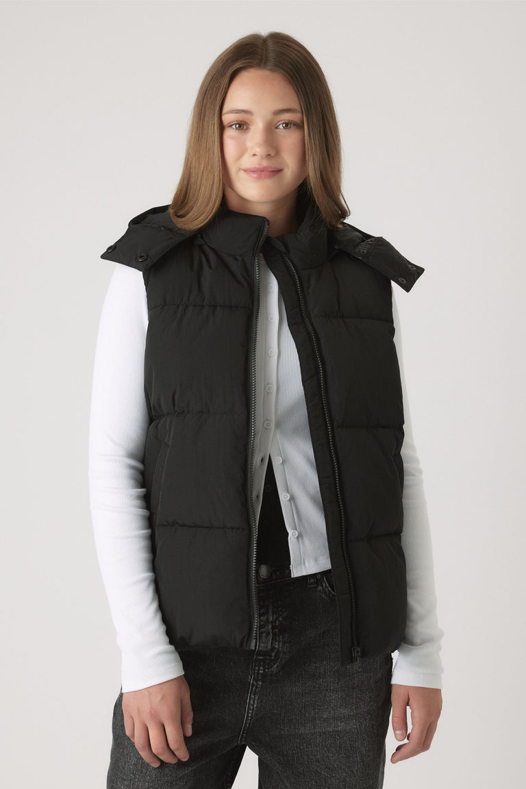 Girl wearing black Girls Hooded Puffer Vest layered over white long sleeve top and dark denim jeans by DECJUBA.