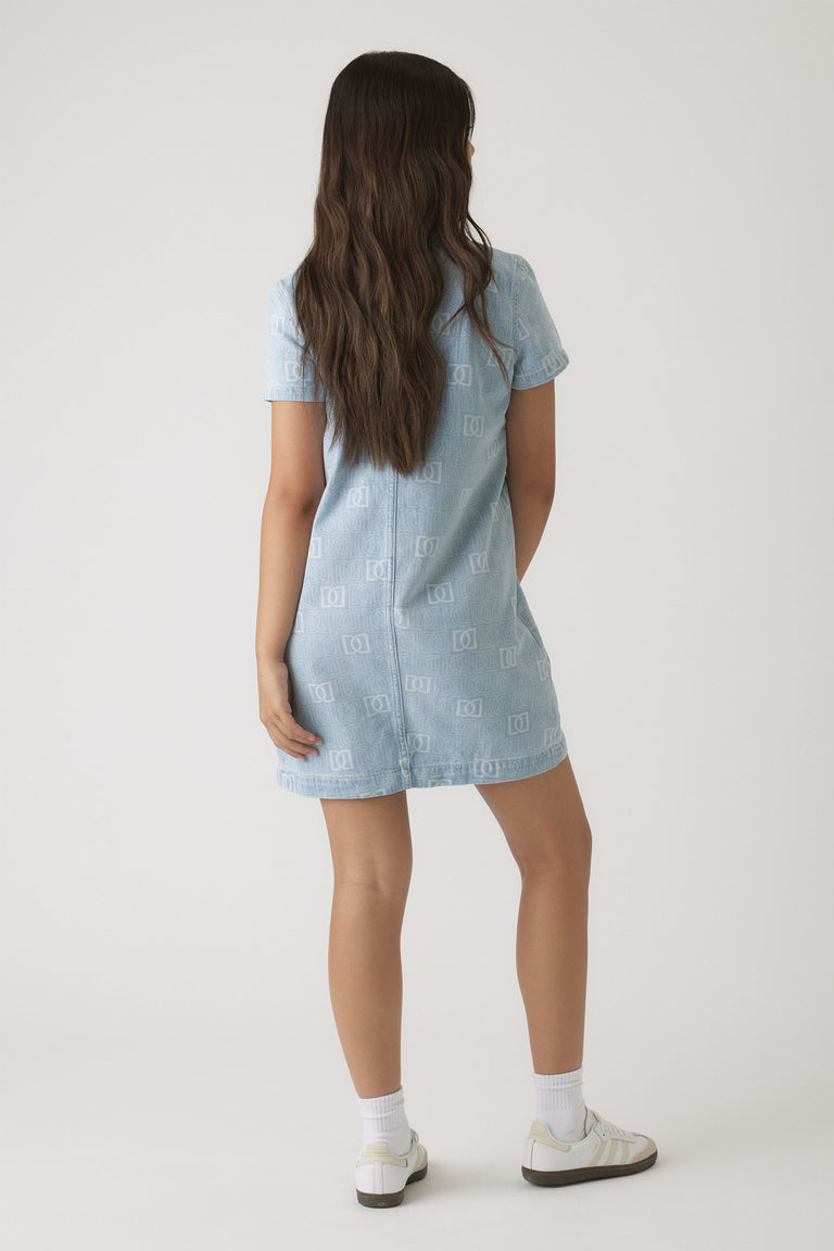 Girl wearing a light wash denim dress with short sleeves and subtle monogram print, paired with white socks and sneakers