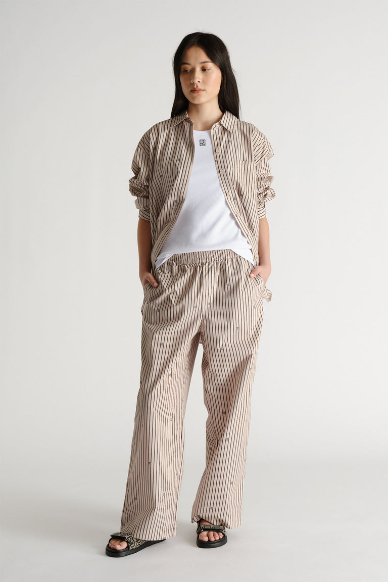 Woman wearing beige monogram stripe pants and matching shirt over a white tee, styled with black sandals.