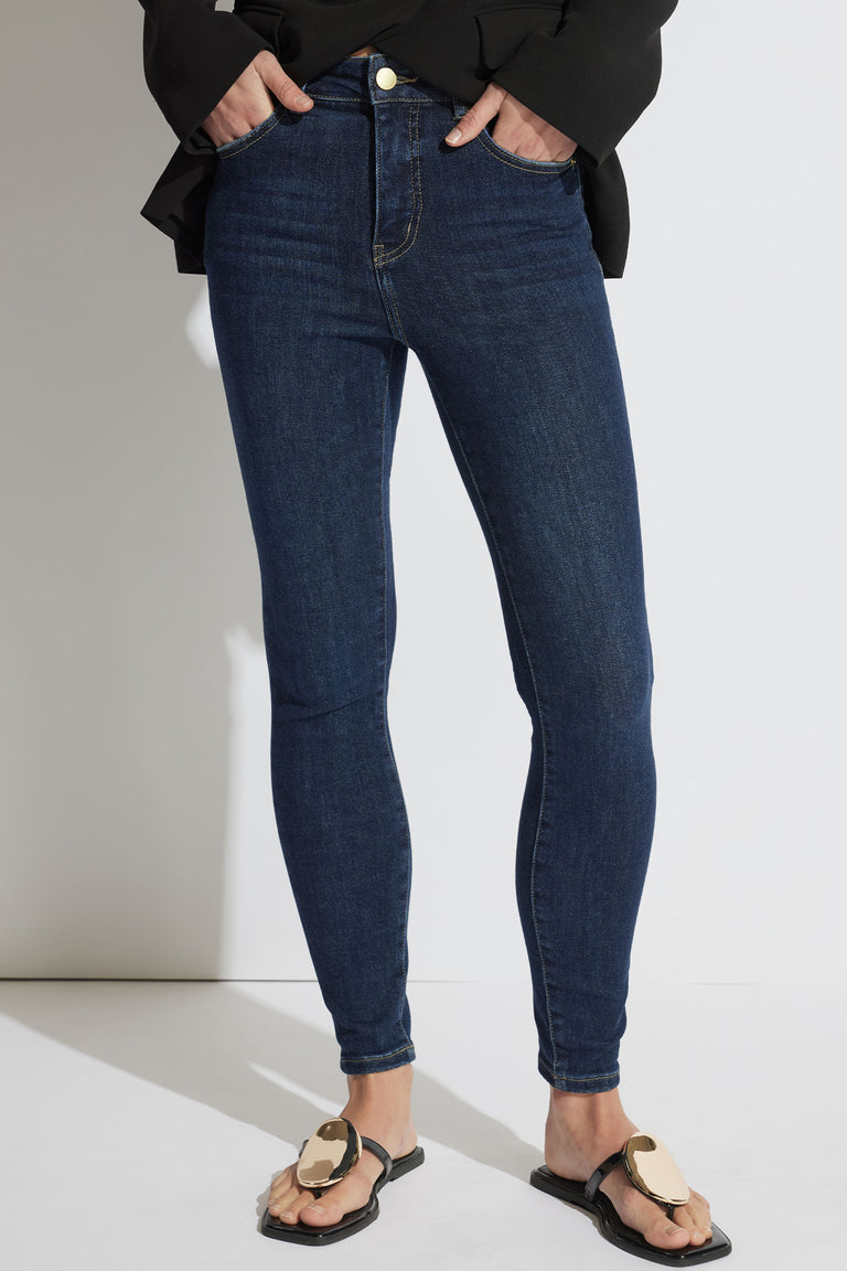 Woman wearing fitted dark blue high-rise skinny jeans styled with a black top and flat sandals for a casual look