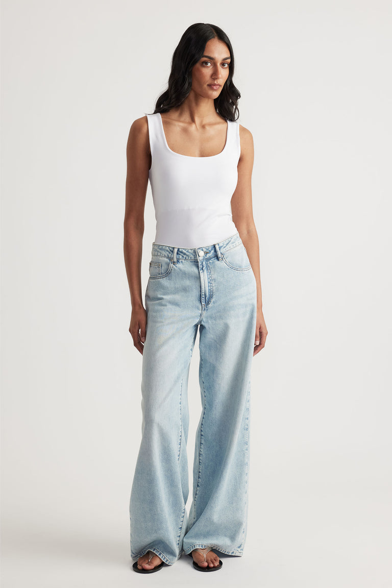 Woman wearing a white seamless scoop tank with light wash wide-leg jeans for a laid-back, versatile look.