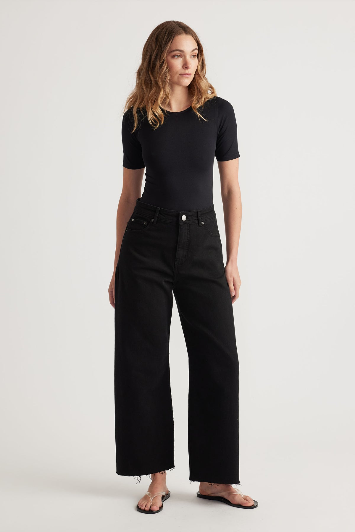 Woman wearing a fitted black short-sleeve top paired with wide-leg black jeans and black flip-flop sandals.