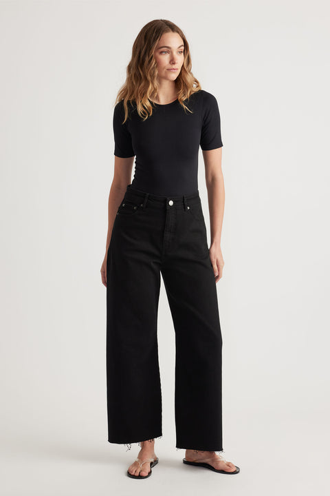 Woman wearing a fitted black short-sleeve top paired with wide-leg black jeans and black flip-flop sandals.