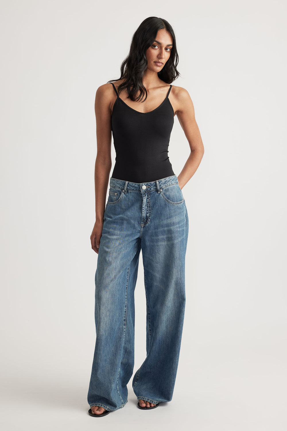 Woman wearing a fitted black thin strap tank paired with relaxed wide-leg blue jeans and black open-toe sandals