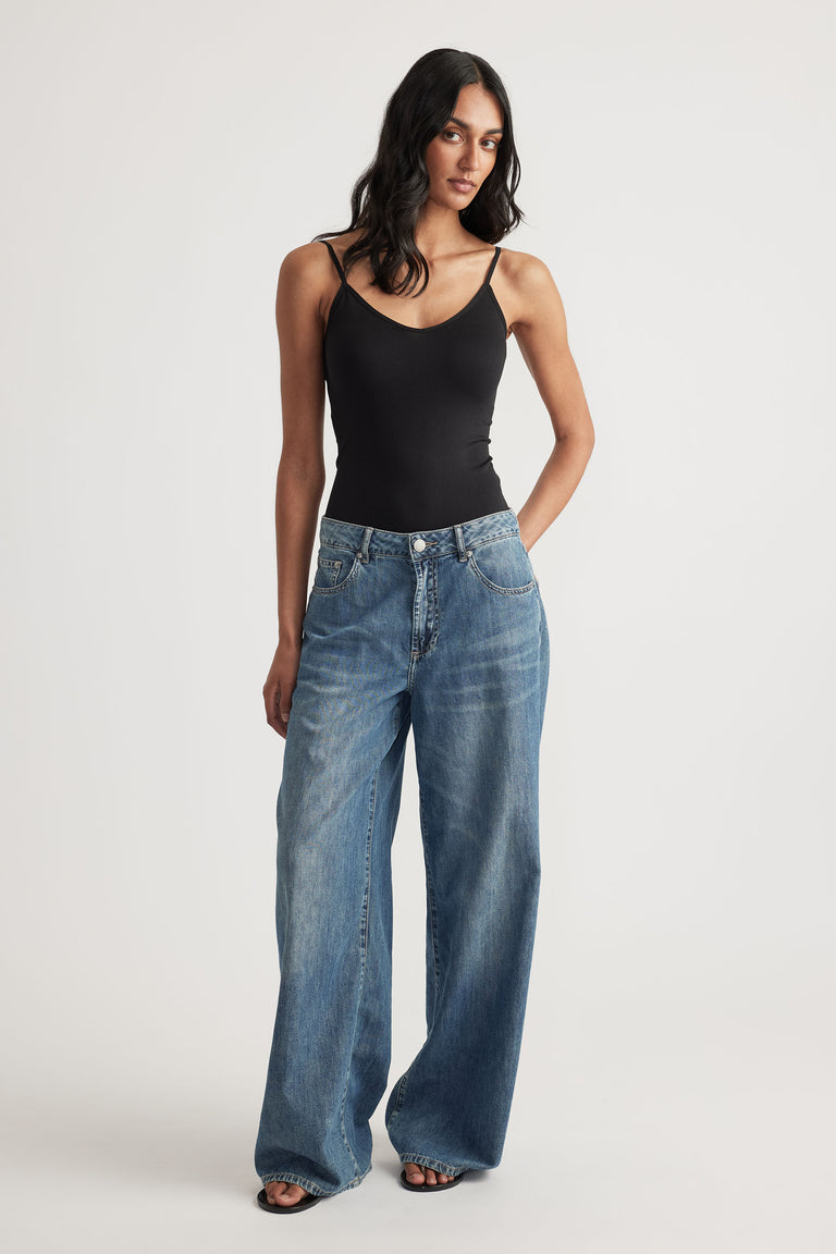Woman wearing a fitted black thin strap tank paired with relaxed wide-leg blue jeans and black open-toe sandals
